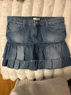Blå volangkjol i denim - Jättefin jeanskjol med volang som tyvärr inte kommer till användning, använd fåtalet gånger och som ny! Storlek 170 men skulle säga att den är som en S