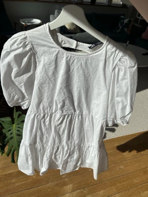 Vit kort klänning från Zara - Superfin vit kort klänning från Zara med puffärmar och öppen rygg. Klänningen har volangdetaljer och knyt i ryggen, vilket ger en söt och trendig look. Perfekt för varma dagar och somriga vibes.