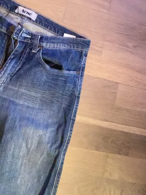 Blå raka jeans från Acne Studios - Säljer ett par klassiska blå jeans från Acne Studios med raka ben och snygg slitning. Jeansen har fem fickor, normal midja och är tillverkade i denim. Perfekta för en avslappnad och trendig look. Storlek 31/32