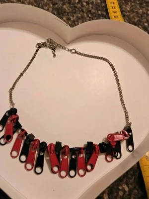 Halsband med svarta och rosa dragkedjor - Unikt halsband med kedja i metall och dekorationer av svarta och rosa dragkedjor. Kedjan är silverfärgad och dragkedjorna hänger tätt i ett mönster som ger ett edgy och kreativt uttryck. Perfekt för dig som gillar att sticka ut och vill ha något annorlunda.