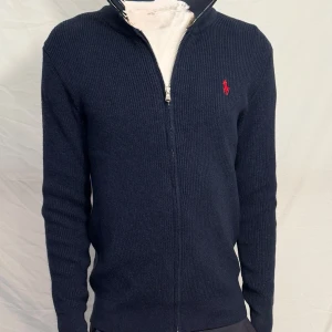 Ralph lauren tröja - Stilren mörkblå zip-kofta från Ralph Lauren i fint skick. Ribbstickad design med dragkedja och klassisk broderac logga på bröstet. Pris går att diskuteras