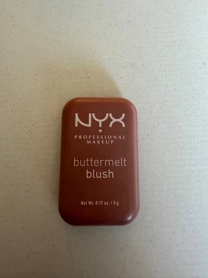 NYX buttermelt blush i brunrosa nyans - NYX Professional Makeup buttermelt blush i en snygg brunrosa nyans. Kommer i en smidig, rektangulär dosa med lock. Rouget har en mosaikmönstrad yta och är i puderform, perfekt för att ge kinderna en naturlig glow.