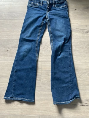 Blå bootcut jeans från Gina Tricot - Säljer ett par blå bootcut jeans från Gina Tricot med snygga kontrastsömmar och klassisk femficksmodell. Jeansen har utsvängda ben och normal midja, perfekta för en trendig och avslappnad look. Det är lite trasiga längst ner som man ser på bilden 