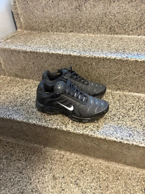 Nike TN UTILITY - Säljer ett par Nike Air Max Plus Tn sneakers i svart mesh med vita detaljer och Tn-logo på hälen. Skorna har en sportig design med synlig Air-dämpning och coola reflexdetaljer. Perfekt för dig som gillar streetstyle och vill ha något bekvämt och snyggt.