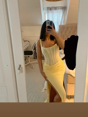 Ljusgul långklänning med slits - Säljer nu en supersnygg ljusgul långklänning från oh polly med figurnära passform och korset. Klänningen har breda axelband, korsettliknande överdel och en slits på sidan. Materialet är ganska stretchigt, perfekt för sommarkvällar och baler💛