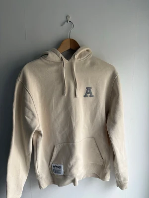Beige Axel Arigato hoodie - Säljer denna fräscha beiga Axel Arigato hoodien. Perfekt för vår och sommar. Plagget är i mycket bra skick då den endast har ett litet märke på ryggen. Storlek S