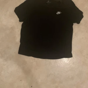 Svart Nike t-shirt med logga - Snygg svart t-shirt från Nike med klassisk vit logga på bröstet. T-shirten har korta ärmar och en enkel, clean design som passar till det mesta. Perfekt för dig som gillar sportiga och stilrena plagg.