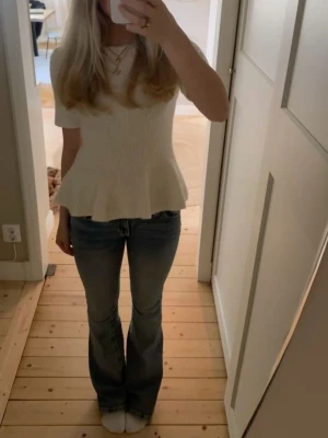 Vit ribbad topp med volang - Säljer en söt vit topp med ribbad struktur och volang nedtill. Toppen har korta ärmar och en figurnära passform upptill som släpper ut i en peplumvolang. Perfekt att styla med jeans eller kjol.