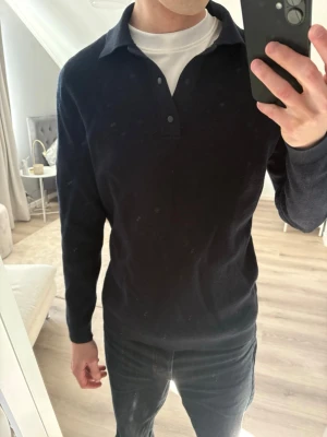 Marinblå pikétröja från Mango - Snygg marinblå långärmad pikétröja från Mango med klassisk krage och tre knappar framtill. Tröjan har en diskret struktur i materialet och passar perfekt till både jeans och chinos. Enkel och stilren design som funkar till många olika looks.