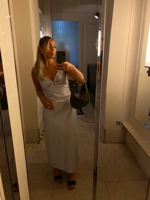 Ljuslila långklänning 💜 - Säljer min eleganta Adoore långklänning med v-ringad hals och smala axelband med rynkade detaljer. Klänningen har en figurnära passform och är tillverkad i ett silkesmaterial. Enbart använd för ett bröllop! Fint skick. Stl 42. 