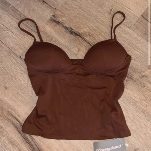 Brun croppad linnetopp från Missguided - Snygg brun croppad linnetopp från Missguided med smala axelband och vadderade kupor. Toppen har en figurnära passform och är perfekt för att styla med höga jeans eller kjol. Enkel men trendig design som passar till många looks.