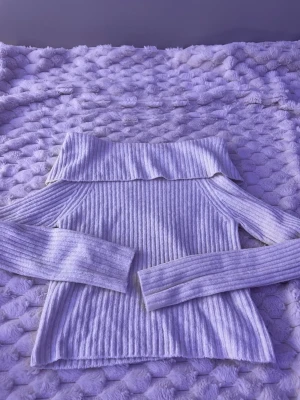 Ljuslila ribbstickad tröja - Trendig ljuslila ribbstickad tröja med bred polokrage och långa ärmar. Tröjan har en figurnära passform och är tillverkad i ett mjukt, stretchigt material som känns skönt mot huden. Perfekt för dig som gillar en stilren och modern look.