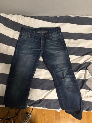Mörkblå jeans från Jack n Jones - Säljer ett par mörkblå jeans från Jack n Jones med klassisk femficksmodell och snygga slitningar framtill. Jeansen har en rak passform och är tillverkade i kraftigt denimtyg. Perfekta för en avslappnad och stilren look.