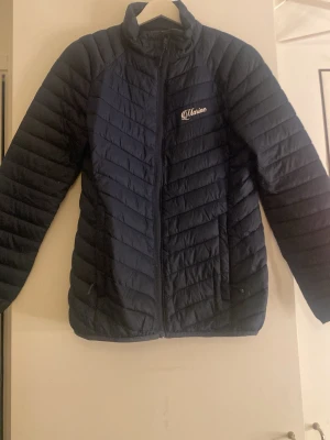 Mörkblå pufferjacka från Marine  - Snygg mörkblå pufferjacka från marine med quiltad design och dragkedja framtill. Jackan har lång ärm och står upp i kragen för extra värme. Perfekt för kyliga dagar och enkel att matcha med olika outfits.