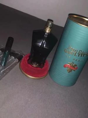 Jean Paul Gaultier Le Beau Parfum - Säljer en Jean Paul Gaultier Le Beau Parfum i en unik svart flaska formad som en manlig torso med gulddetaljer. Kommer med original grön metalltub och röd sammetsbas. En elegant och lyxig parfym som sticker ut i badrumshyllan.