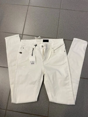 Vita slim fit jeans från tiger of Sweden  - Snygga vita slim fit jeans från tiger of Sweden  med klassisk femficksmodell och raka ben. Jeansen har bälteshällor, knappgylf och är tillverkade i ett mjukt bomullsmaterial. Perfekta för dig som vill ha en clean och fräsch look.