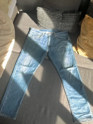 Blå Levi's jeans raka ben - Säljer ett par klassiska blå Levi's jeans med raka ben eftersom dom var för stora för mig. Jeansen har en ljus tvätt och är tillverkade i slitstark denim. Typisk Levi's-detalj med röd etikett på bakfickan och läderpatch i midjan.