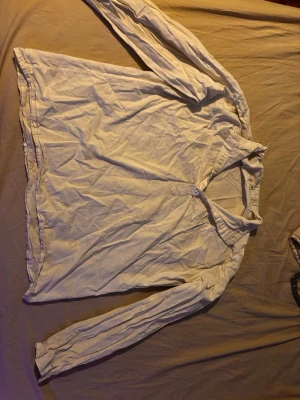 Vit långärmad henley skjorta - Klassisk vit henley skjorta med lång ärm och krage. Skjortan har knappar framtill och är tillverkad i ett mjukt bomullstyg. Enkel och stilren design som passar till många olika looks.