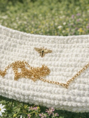 Vit virkad kuvertväska med guldkedja - Superfin vit kuvertväska i virkat material med en snygg guldfärgad kedja och en dekorativ bi-detalj framtill. Perfekt accessoar för att lyfta vilken outfit som helst. Väskan har en mjuk struktur och stängs med lock.