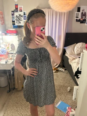 Svartvit fjärils kortklänning - Supersöt svartvit kortklänning med små fjärilar och puffärmar. Klänningen har en söt snörning framtill vid bysten och en lätt v-ringad urringning. Passformen är normal och materialet känns som mjuk bomull eller polyester. Perfekt för sommarens alla tillfällen!