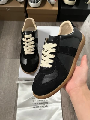 Maison Margiela svarta sneakers - Svarta sneakers från Maison Margiela med beigea skosnören och klassisk gummisula🤩 Storlek 41 i fint skick. Hör av er vid funderingar samt snabbaffär😇