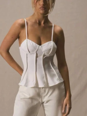 Vit bustierlinne med smala axelband - Säljer ett vitt bustierlinne med smala, justerbara axelband och markerade sömmar framtill. Toppen har en figurnära passform och lätt utsvängd nederkant. Perfekt att styla med jeans eller kjol för en trendig look.