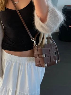 Bucketbag från H&M - Snygg axelväska med flätad design i brunt läder och beige påse. Väskan har justerbar axelrem, dragskostängning och kontrastsömmar. Det finns tecken på användning, allt går att se på bilderna. 