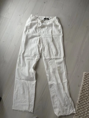 Vita linnebyxor - Säljer ett par vita linnebyxor med avslappnad passform och dragsko i midjan. Byxorna har raka ben och är tillverkade i ett lätt och luftigt linnetyg, perfekta för en chill och stilren look. Jag är cirka 172 cm men kan också sys upp. 