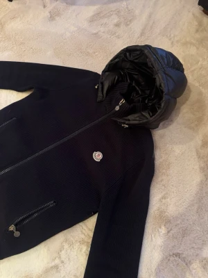 Moncler cardigan! - Snygg mörkblå cardigan från Moncler med glansig vadderad huva och rygg, samt stickade ärmar och framstycke. Jackan har två dragkedjefickor fram och Moncler-logga på bröstet. Storlek XL men sitter som en M, passar perfekt på mig som är 180, bild kan skickas! Perfekt för höst vår sommar dagar och riktigt trendig look! Säljes för 4499 pris kan diskuteras!🤝