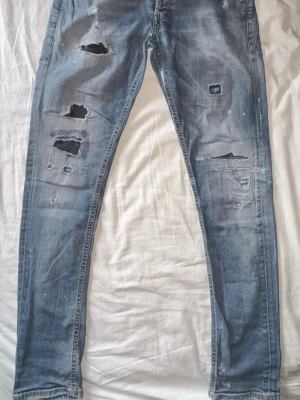 Dondup - Säljer ett par blå skinny fit jeans från dondup som är modelen George med flera slitningar och hål på benen för en trendig, avslappnad look.   
