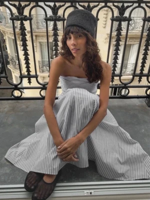 Randig axelbandslös långklänning - Axelbandslös långklänning med smala grå och vita ränder. Klänningen har en figurnära överdel och ett långt, utsvängt kjolparti. Tillverkad i ett lätt och luftigt bomullsmaterial, perfekt för varma dagar.