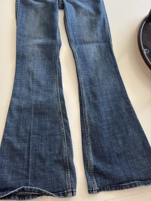 Blå bootcut jeans Hollister - Snygga blå bootcut jeans med klassisk femficksdesign och lätt slitning. Jeansen har utsvängda ben och normal midja, perfekta för en avslappnad och trendig look. Tillverkade i denim med kontrastsömmar.
