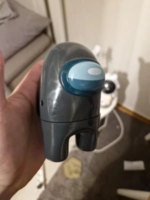 Among Us figur i plast - Säljer en grå och blå Among Us-figur i plast. Figuren har den klassiska runda formen med ben och ett blått visir framtill, inspirerad av spelet Among Us. Perfekt som dekoration eller samlarpryl för fans av spelet.