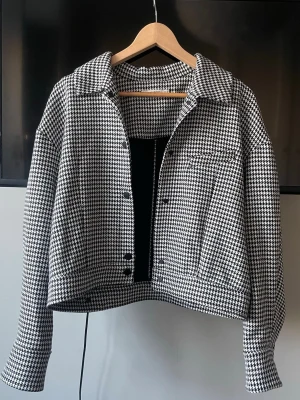 Svartvit hundtandsmönstrad jeansjacka - Snygg svartvit jeansjacka med klassiskt hundtandsmönster. Kortare modell med raka ärmar och krage, knäpps med svarta knappar framtill. Köpt secondhand men har aldrig använt själv. Storlek M men passar också bra för någon som har XS/S❣️