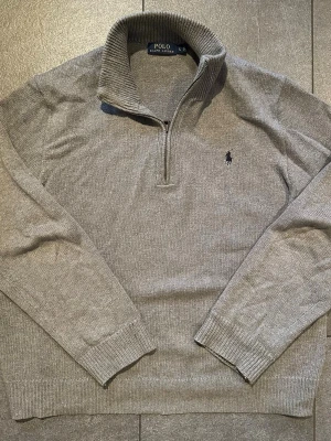 Grå stickad tröja Polo Ralph Lauren - Snygg grå stickad tröja från Polo Ralph Lauren med halv dragkedja och hög krage. Tröjan är i bra skick men är något uttöjd (se bilder för mått). Nypris ligger runt 2500kr