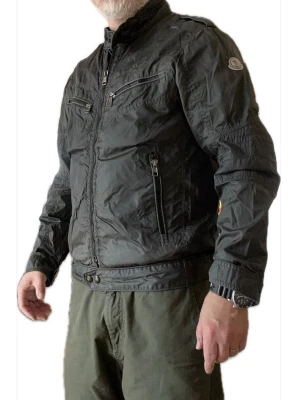 Grå vindjacka från Moncler - Snygg grå vindjacka från Moncler med hög krage, flera dragkedjeförsedda fickor och Moncler-logga på ärmen. Jackan har en sportig look, justerbara muddar och är tillverkad i ett lätt, glansigt material som står emot vind. Perfekt för dig som gillar streetwear och stilren design.