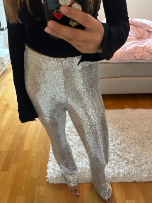 Silvriga paljettbyxor med rak passform - Glittra loss i dessa silvriga byxor täckta med paljetter. Byxorna har rak passform och hög midja, perfekta för dig som vill sticka ut. Materialet är syntet och de har en riktigt snygg och trendig look.
