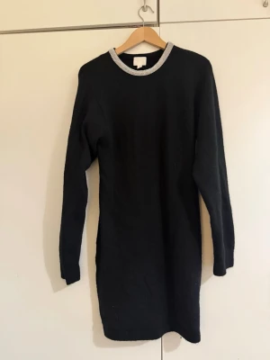 Svart stickad klänning med silverkant - Svart stickad klänning med lång ärm och rund halsringning som har en snygg silverfärgad kant. Enkel och stilren design som passar perfekt till sneakers eller boots.