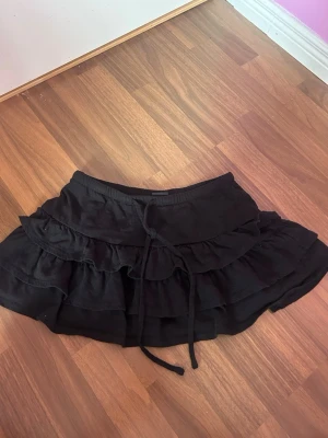 Svart volangkjol från Gina Tricot - Supersöt svart kortkjol från Gina Tricot med volanger och snörning i midjan💗