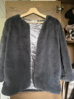 Grå pälsjacka från MissKoo - Snygg grå pälsjacka från MissKoo med mjukt foder och öppen front. Jackan har en rak passform och är gjord i fuskpäls som känns lyxig och varm. Endast testad, kom aldrig till användning för mig :) 