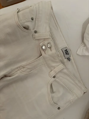 Vita low bootcut jeans - Säljer ett par vita jeans från 157 med snygg dubbelknapp framtill och klassiska femficksdetaljer. Jeansen är bootcut och är tillverkade i ett mjukt denim-material som är bekvämt att bära. Perfekt för dig som gillar stilrena och ljusa jeans. Storlek S - short length 