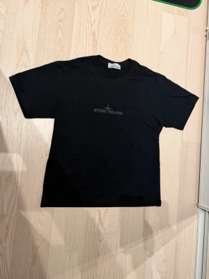 Svart Stone Island t-shirt - Säljer en svart t-shirt från Stone Island med tryckt logga på bröstet och stort grafiskt tryck på ryggen. Klassisk passform med rund hals och korta ärmar. Perfekt för dig som gillar streetwear och vill ha något stilrent men ändå med edge. Sista bilden visar att om man scannar QR koden kommer man dit, pris kan diskuteras