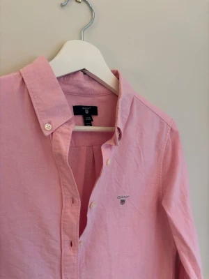 Rosa linne skjorta från Gant - Klassisk rosa skjorta Gant. Skjortan har lång ärm, knappar framtill och en tidlös krage. Passar från 160 till 170 har ingen defekter. Är använd fåtal gånger. Perfekt för sommaren!