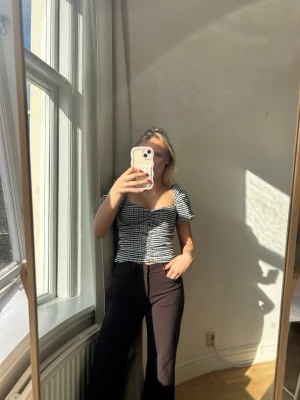 Rutig svartvit blus med puffärm💖✨ - Trendig rutig blus i svart och vitt med puffärmar och söt v-ringning. Toppen har smickrande snörning framtill och är croppad i modellen. Perfekt för dig som gillar en feminin och cool stil.