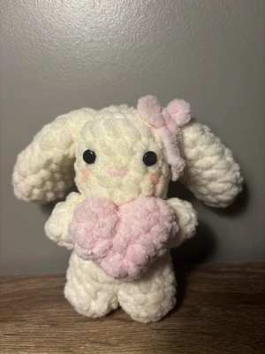 Virkad kanin med rosa hjärta - Supergullig handgjord kanin i mjuk, fluffig vit garn med långa öron och svarta ögon. Kaninen håller ett rosa hjärta och har en matchande rosa rosett på huvudet. Perfekt som dekoration eller present, eller som en liten kompis💞💞💞