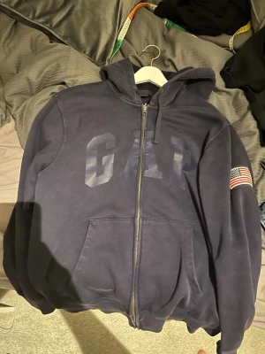 Mörkblå GAP hoodie med dragkedja - Mörkblå hoodie från GAP med dragkedja framtill och stor logga på bröstet. Knappt använd