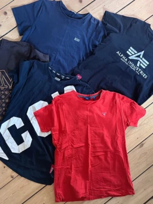 T-shirtpaket Alpha Industries & Gant - Säljer ett paket med fem t-shirts i olika färger och tryck från Alpha Industries, Gant och Nocco. Färgerna är marinblå, svart och röd. Alla t-shirts är kortärmade och i mjuk bomull, perfekta för en avslappnad stil.
