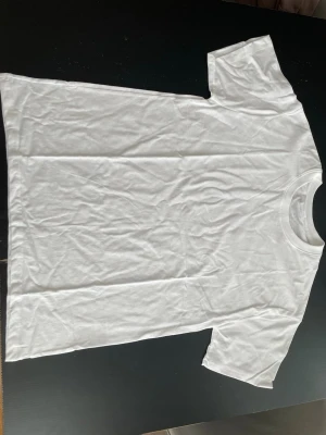 Vit basic t-shirt i bomull - Klassisk vit t-shirt med rund hals och korta ärmar. Tillverkad i mjuk bomull för en skön och avslappnad känsla. Perfekt att matcha med jeans eller shorts för en enkel och clean look. Aldrig använd storleken är L/LARGE
