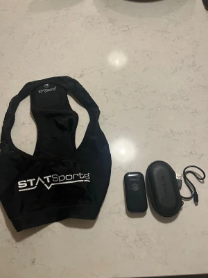 Pulsmätare från STATSports med tillbehör - Pulsmätare från STATSports med svart elastisk sele, sensor, laddkabel och skyddsfodral. Perfekt för träning och sport, enkel att använda och smidig att bära under kläder. Snygg design med tydlig logga på selen. Nypris 4000 kr använt ett tiotal gånger men funkar perfekt. Smidig att koppla ihop på Statsports appen. 