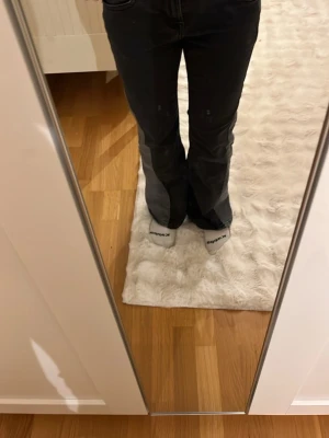 Svarta bootcut jeans med fickdetaljer - Säljer ett par svarta bootcut jeans med snygga fickdetaljer bak och silverfärgade knappar. Jeansen har en klassisk femficksmodell och är tillverkade i ett stretchigt denimtyg som sitter bekvämt. Perfekta för en trendig och avslappnad look.